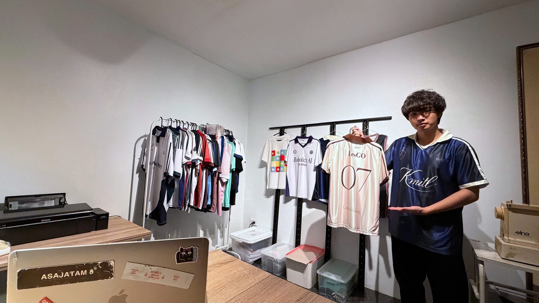 The LESGO founder holding up a jersey in the studio, with racks of finished shirts behind him